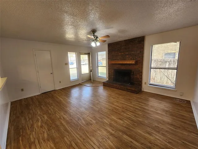 an empty room with wooden floor fireplace and windows