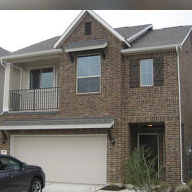 View of front of house with driveway, brick siding, a garage, and a balcony
