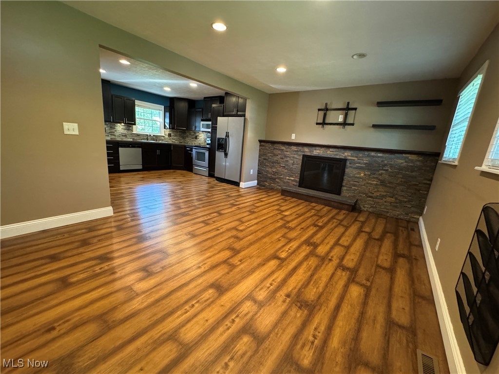 Living room with a stone fireplace, wood-style laminate floors, recessed lighting, and open to kitchen.