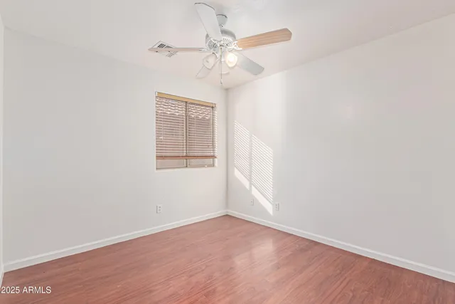 an empty room with wooden floor fan and windows