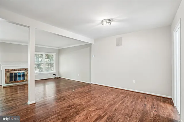 a view of an empty room with wooden floor fireplace and a window