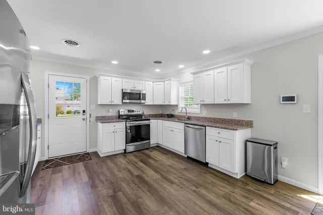 a kitchen with granite countertop a refrigerator oven a sink dishwasher white cabinets and wooden floor