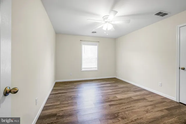 an empty room with wooden floor chandelier fan and windows