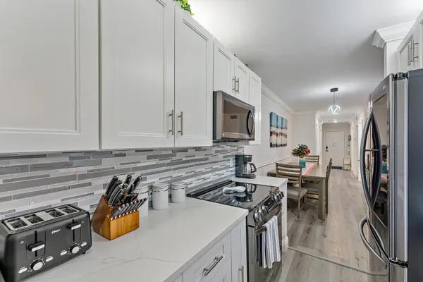 a kitchen with stainless steel appliances a stove a sink dishwasher a refrigerator and white cabinets with wooden floor