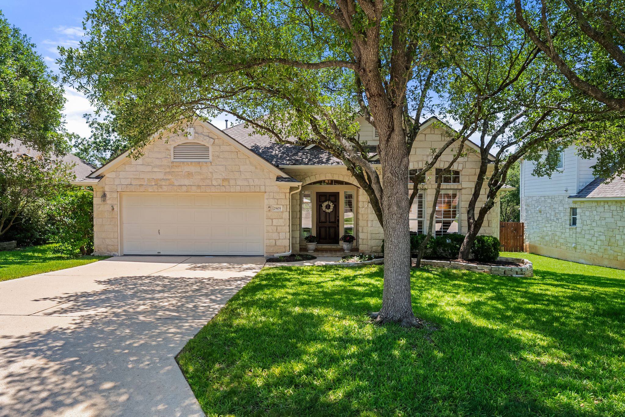 2905 Grimes Ranch Road Austin, TX 78732 - Photo 1 of 1 Stone facade home featuring an attached garage, a paved driveway, and mature trees