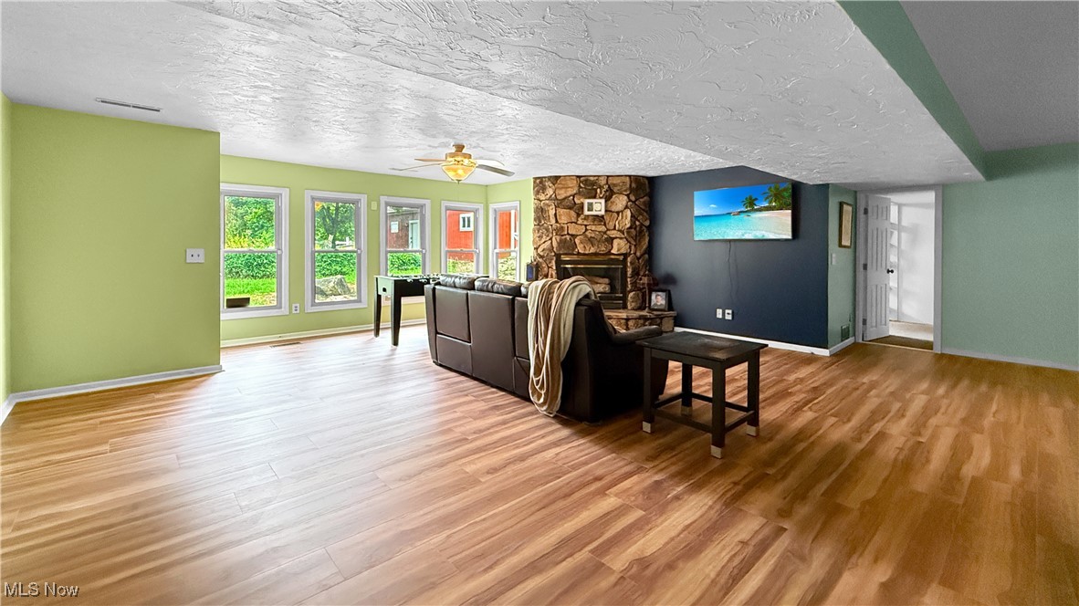 2784 Frost Road Mantua, OH 44255 - Photo 28 of 36 Recreation room featuring a textured ceiling, a stone fireplace, light wood-style flooring, and ceiling fan