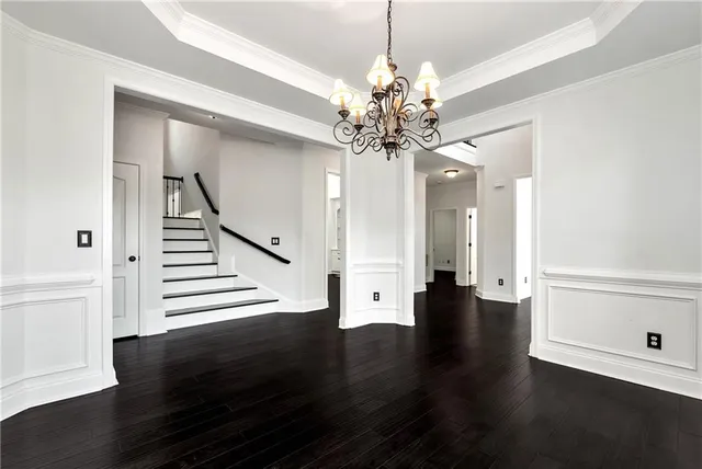 a view of an empty room with chandelier and wooden floor
