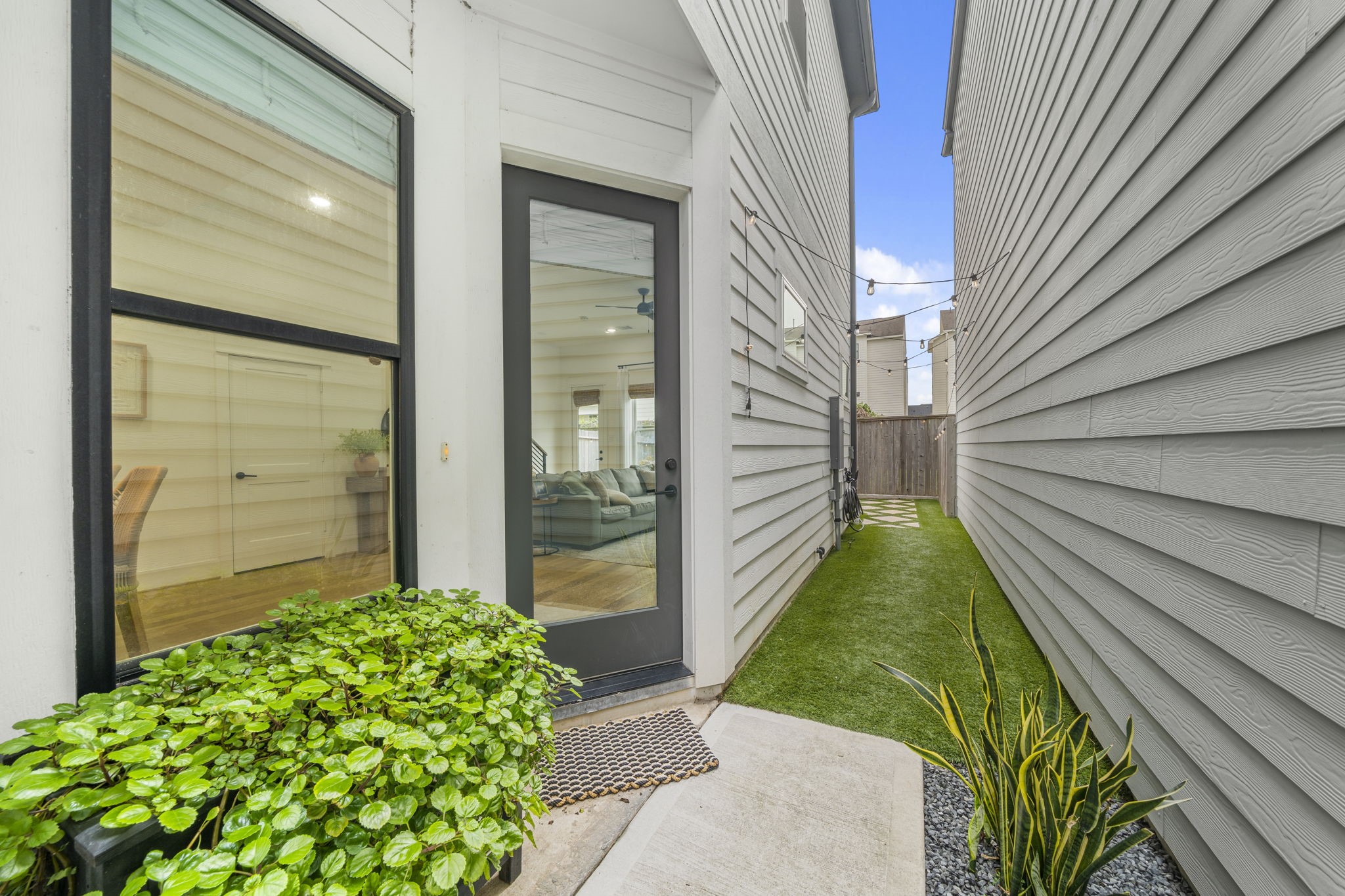 9018 Wellspring Drive Houston, TX 77080 - Photo 3 of 25 A sleek, full-glass back door provides a seamless transition from the interior living space to the side garden and artificial lawn, accented by festive bistro string lighting for evening ambiance.