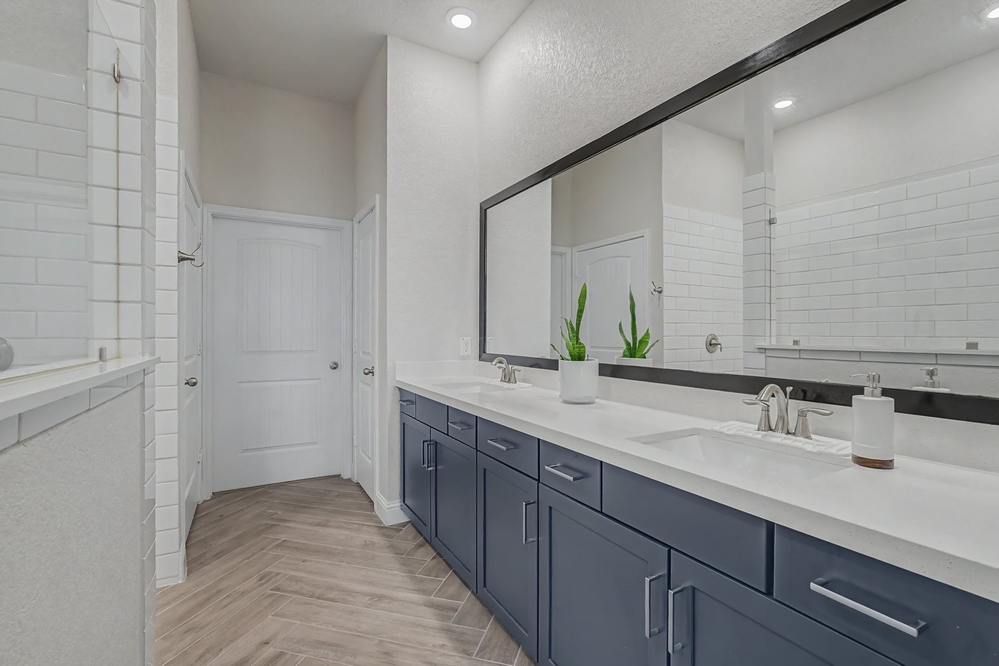 21339 Sierra Point Lane Porter, TX 77365 - Photo 17 of 36 This bathroom features a modern design with a large double vanity, blue cabinetry, white countertops, and a wide mirror. The space is complemented by a walk-in shower with white subway tiles and stylish herringbone-patterned flooring.