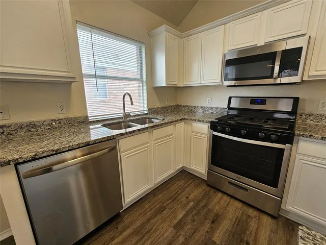 a white kitchen with granite countertop stainless steel appliances and sink