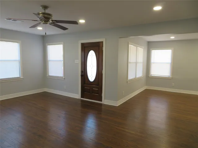 an empty room with wooden floor fan and windows