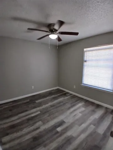 an empty room with wooden floor fan and windows