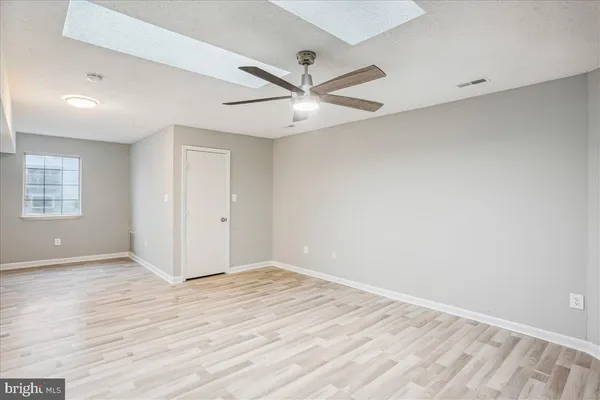 an empty room with wooden floor ceiling fan and windows
