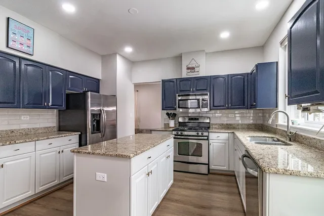 a kitchen with stainless steel appliances granite countertop a stove top oven a refrigerator and a sink with wooden cabinets