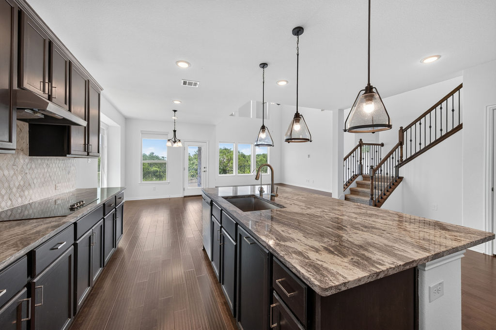 1332 Ridge Runner Drive Georgetown, TX 78628 - Photo 14 of 40 An open concept kitchen features sleek dark cabinetry, granite countertops, and modern pendant lighting, flowing into a spacious living area.