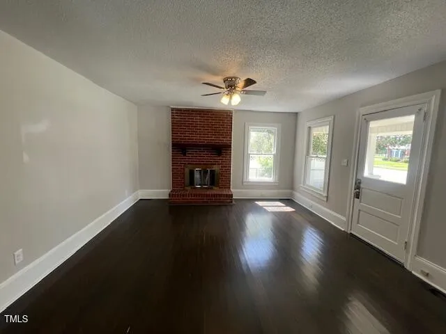 an empty room with wooden floor fireplace and windows