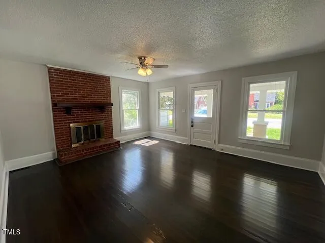 a view of an empty room with wooden floor fireplace and a window