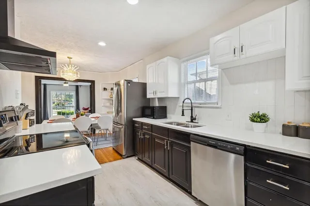 a kitchen with stainless steel appliances a sink dishwasher a refrigerator a stove and white cabinets with wooden floor