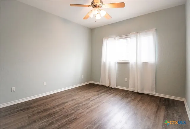 an empty room with wooden floor fan and windows