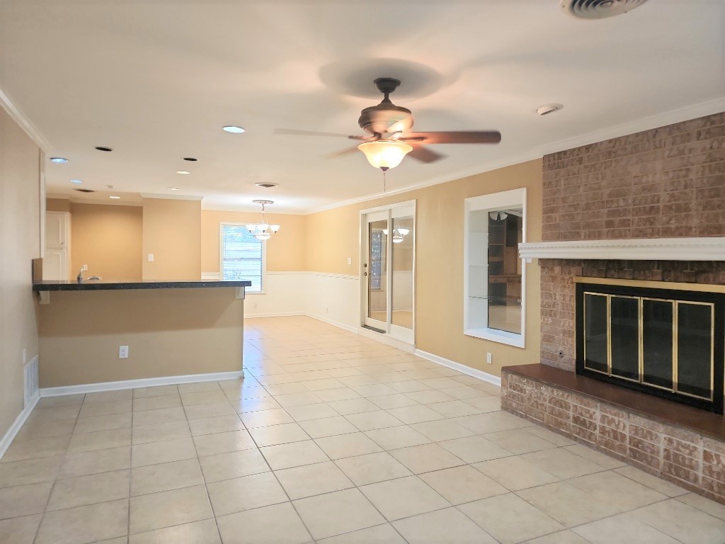 807 Country Club Road Georgetown, TX 78628 - Photo 6 of 31 Unfurnished living room with crown molding, light tile patterned flooring, a brick fireplace, a ceiling fan, and a chandelier