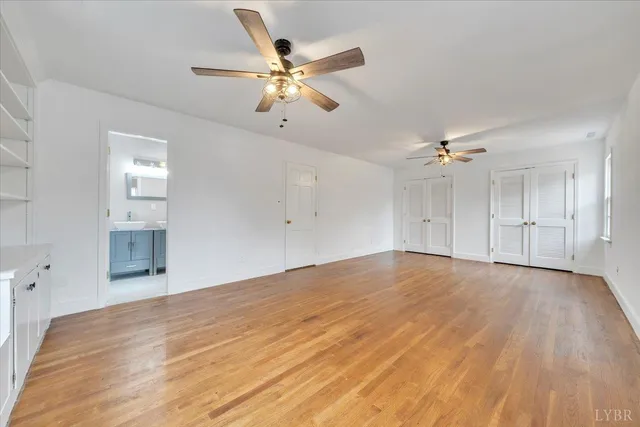 an empty room with wooden floor chandelier fan and windows
