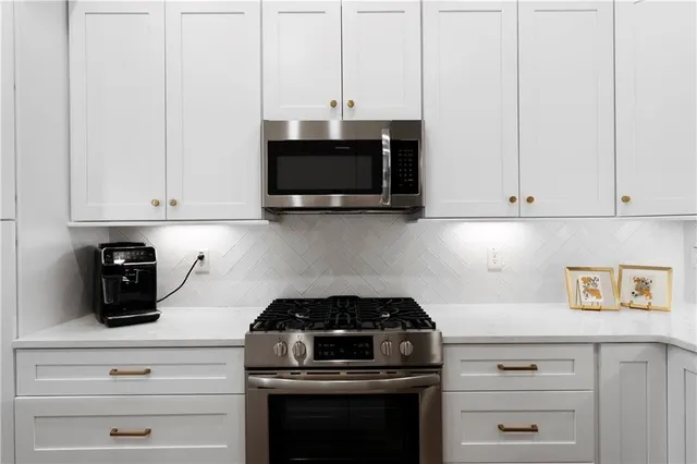 a kitchen with stainless steel appliances granite countertop white cabinets and a stove top oven