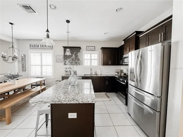 a kitchen with kitchen island granite countertop a refrigerator a sink dishwasher a stove and white cabinets with wooden floor