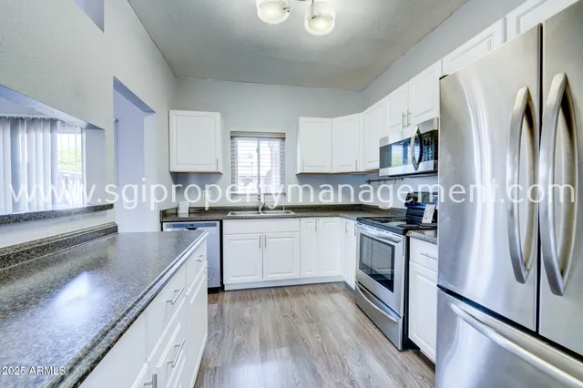 a kitchen with stainless steel appliances granite countertop a refrigerator a stove a sink and white cabinets with wooden floor