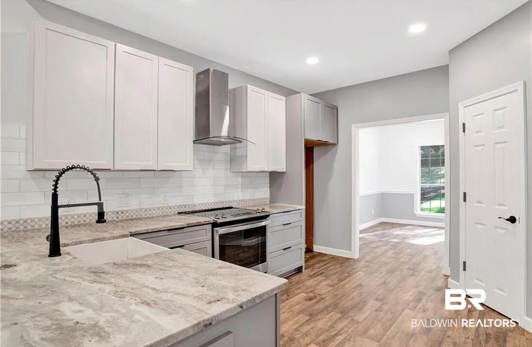 632 Ridgewood Drive Daphne, AL 36526 - Photo 12 of 36 Kitchen with sink, stainless steel range with electric stovetop, white cabinetry, light stone counters, and wall chimney exhaust hood