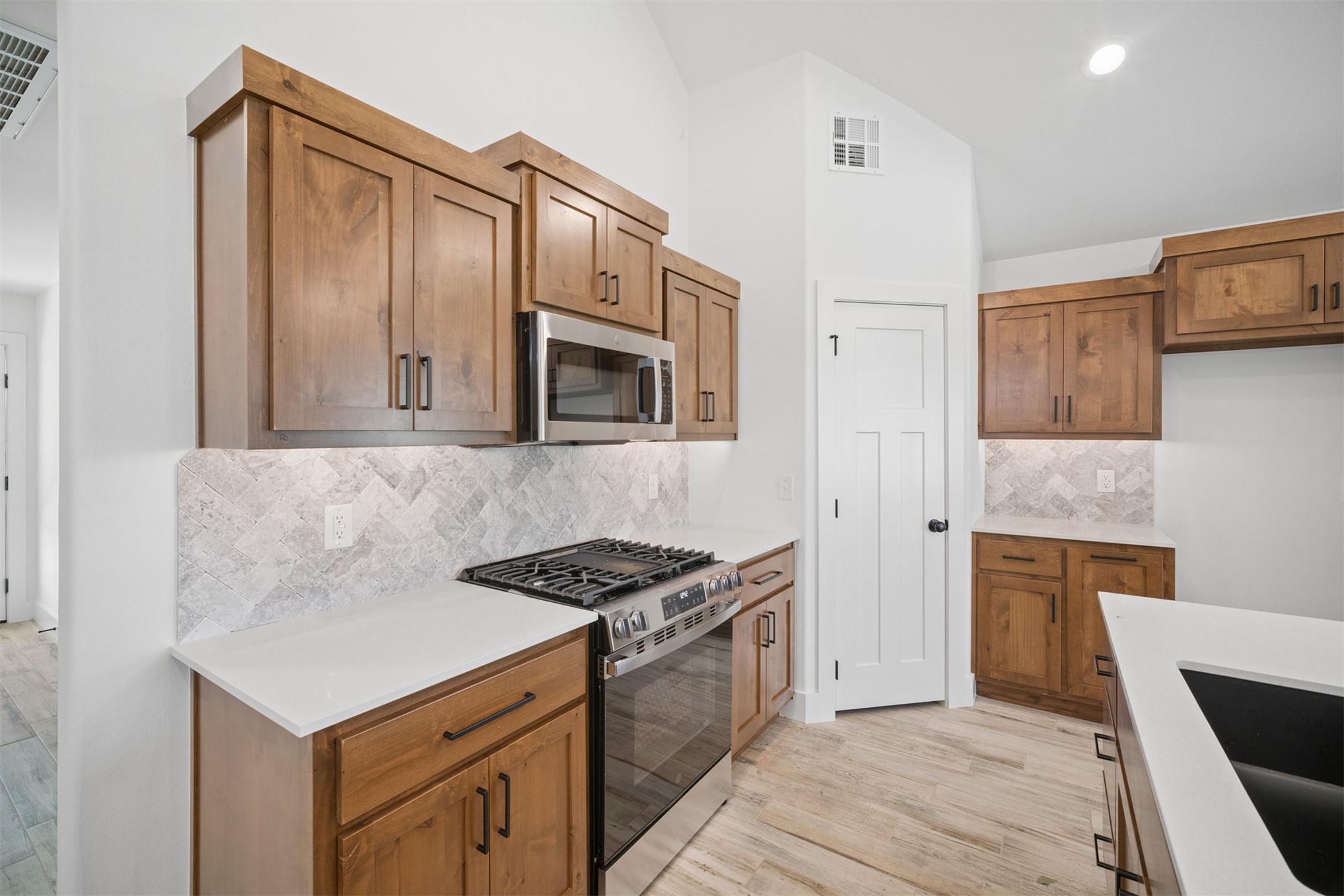 25036 South 4205 Road Inola, OK 74036 - Photo 10 of 30 Wood-finish cabinetry, stainless steel appliances, white countertops, tile backsplash, and light wood-finish flooring