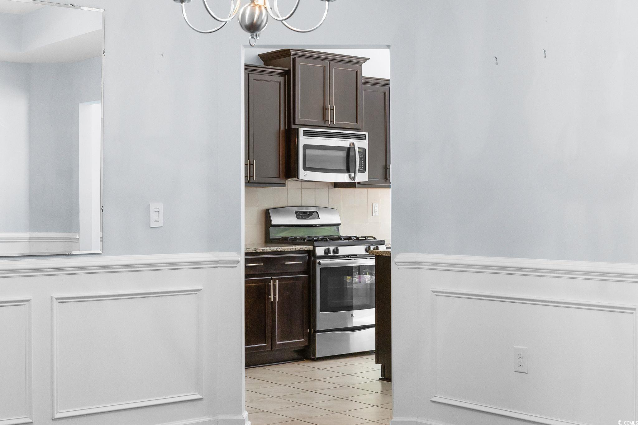 817 Arezzo Way, Unit 1001 Myrtle Beach, SC 29579 - Photo 7 of 40 Kitchen with dark brown cabinetry, backsplash, stainless steel appliances, light tile patterned floors, and wainscoting