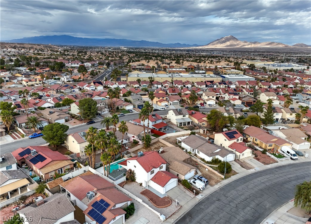 581 Carleton Drive Henderson, NV 89014 - Photo 30 of 37 An aerial panorama reveals a vast residential community nestled beneath distant mountains, dotted with palm trees and a glimmering private pool.
