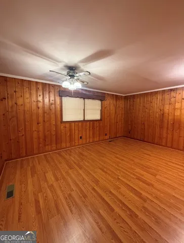 a view of an empty room with wooden floor and a ceiling fan