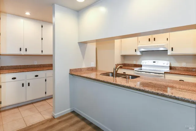 a kitchen with stainless steel appliances granite countertop a sink a stove and white cabinets with wooden floor