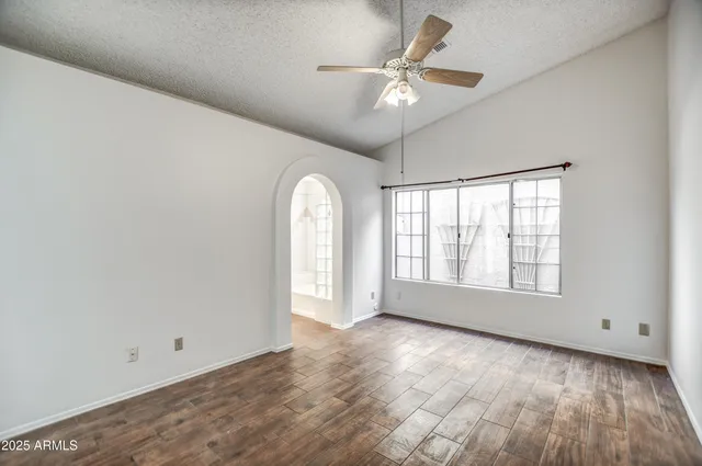 an empty room with wooden floor chandelier fan and windows