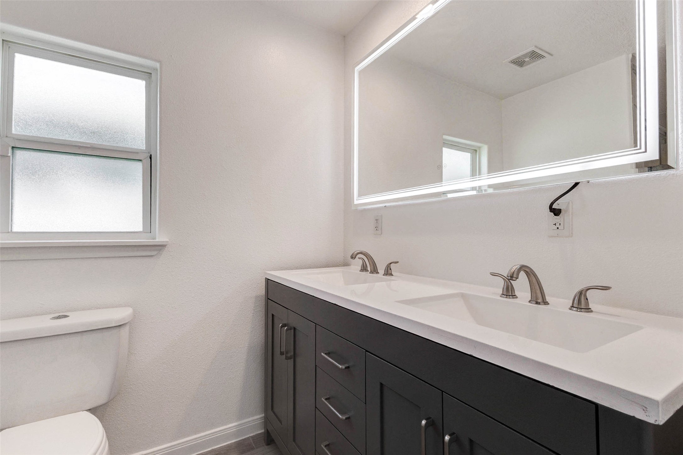 9811 Kerr Street Houston, TX 77029 - Photo 15 of 22 Elegant primary bathroom featuring a stunning walk-in glass shower with large-format marble-look tile that creates a luxurious, spa-like feel. The sleek fixtures and clean glass enclosure add a modern touch, while the spacious dual-sink vanity offers ample storage and countertop space. A large framed mirror and bright lighting enhance the openness of the room, making this beautifully designed space both functional and refined for everyday comfort.