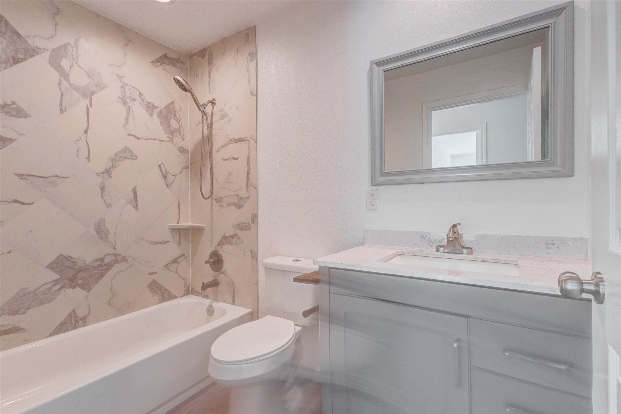 9811 Kerr Street Houston, TX 77029 - Photo 18 of 22 Stylish full bathroom featuring a modern vanity with sleek countertop, updated fixtures, and a beautifully tiled tub and shower combination. The marble-look tile adds a touch of elegance, while the clean design ensures easy maintenance. A well-appointed space that blends comfort, functionality, and contemporary style.