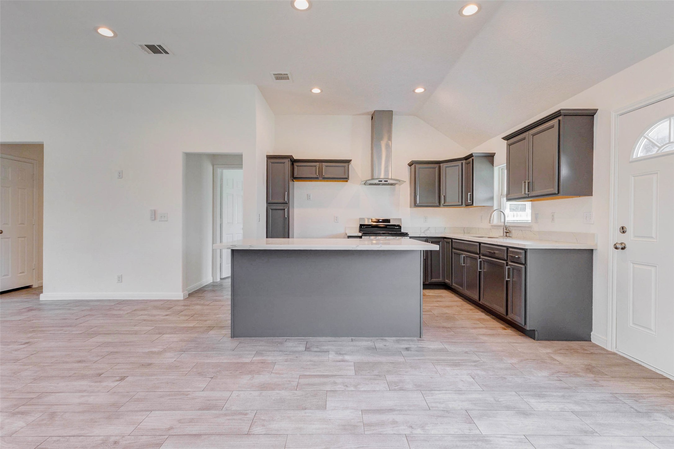 9811 Kerr Street Houston, TX 77029 - Photo 6 of 22 Stunning open-concept kitchen designed for both everyday living and entertaining, featuring a large center island with sleek countertops, rich cabinetry, and a modern vent hood that creates a striking focal point. Recessed lighting and vaulted ceilings enhance the spacious feel, while durable tile flooring flows seamlessly throughout. This inviting layout offers the perfect balance of style and functionality, ideal for gathering with family or hosting guests.