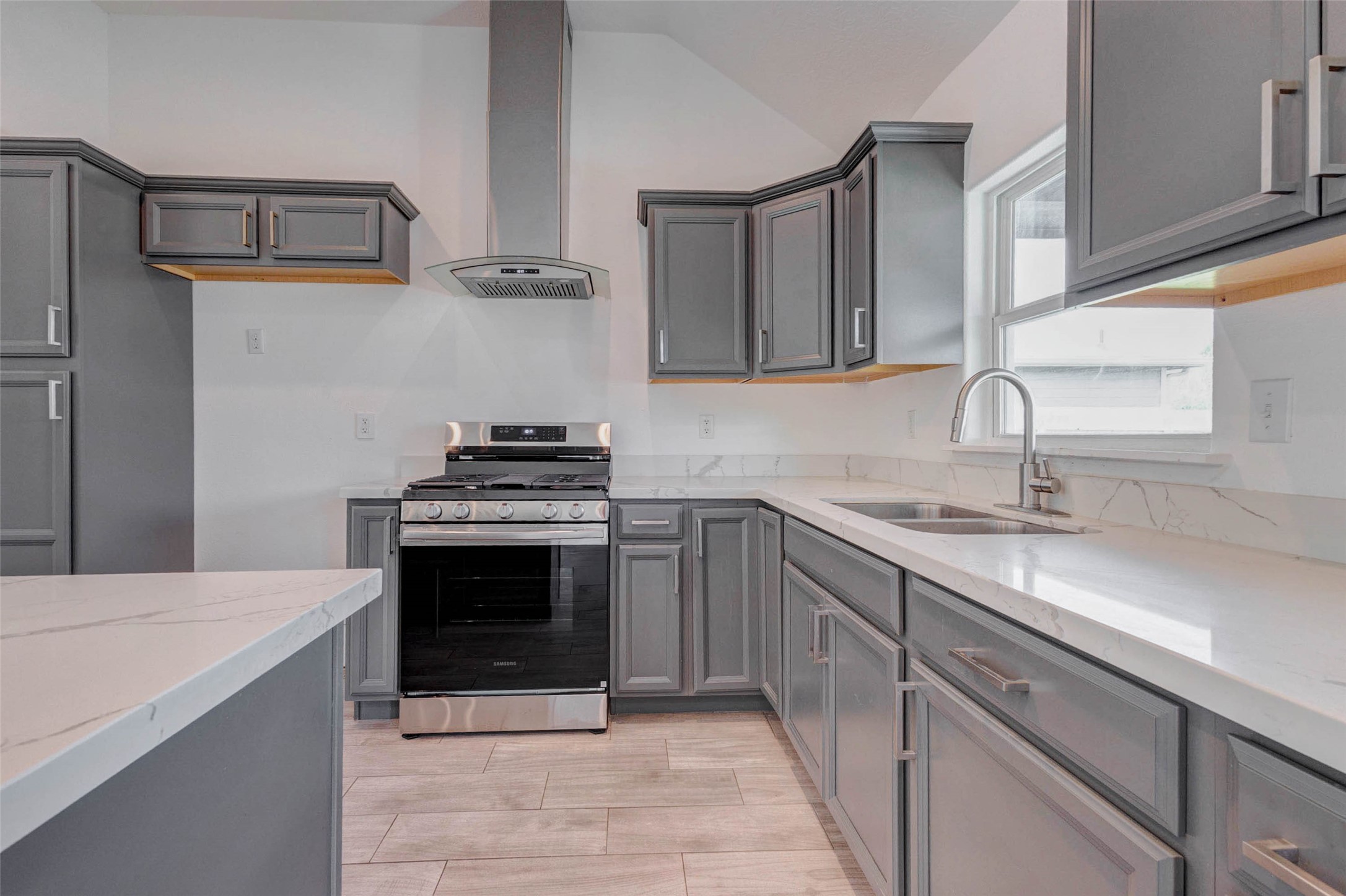 9811 Kerr Street Houston, TX 77029 - Photo 8 of 22 Beautifully designed kitchen featuring sleek countertops, modern gray cabinetry, and stainless steel appliances. The stylish vent hood and tile backsplash create a contemporary focal point, while the window above the sink brings in natural light. Ample cabinet space and thoughtful layout make this kitchen both functional and visually appealing, ideal for everyday cooking and entertaining alike.