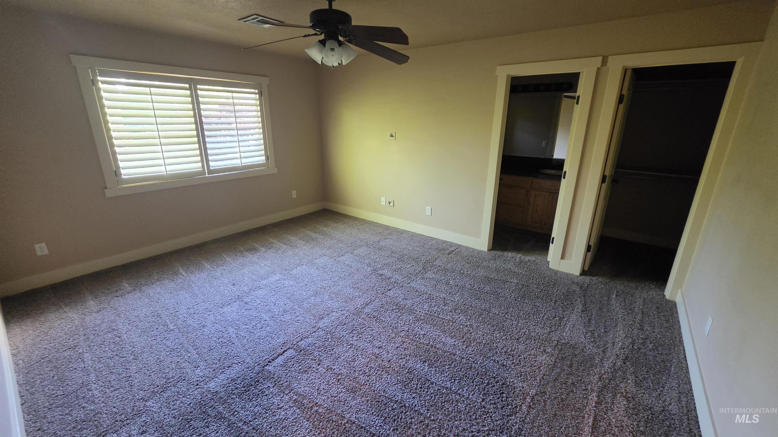 5239 West Morris Hill Road Boise, ID 83706 - Photo 12 of 19 Spacious carpeted room featuring a ceiling fan with integrated lighting, a window with horizontal blinds, and two doorways, one opening to a vanity area with wood cabinetry