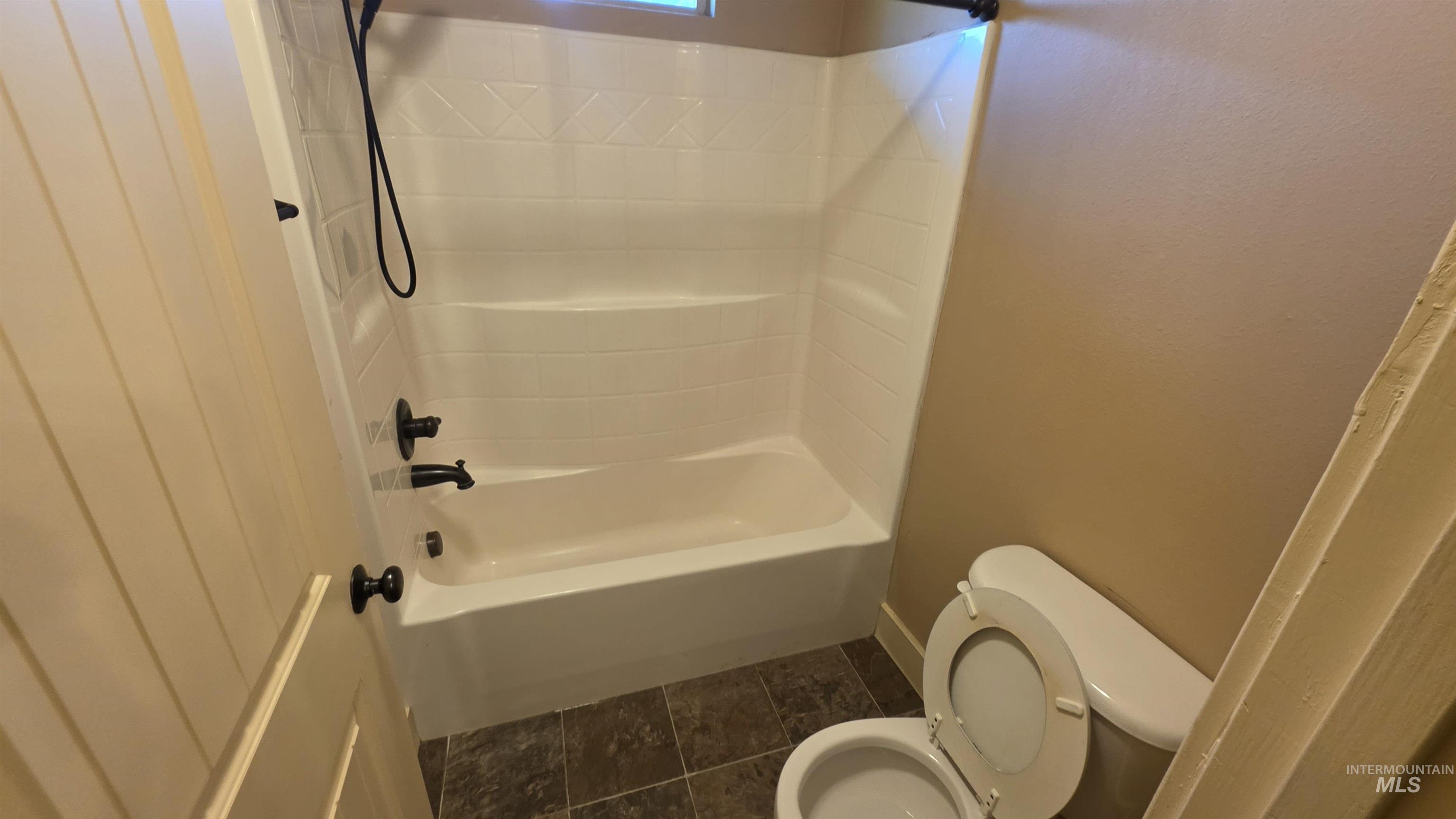 5239 West Morris Hill Road Boise, ID 83706 - Photo 14 of 19 Bathroom featuring a white tub-shower combination with dark bronze fixtures, a white toilet, and dark tile flooring
