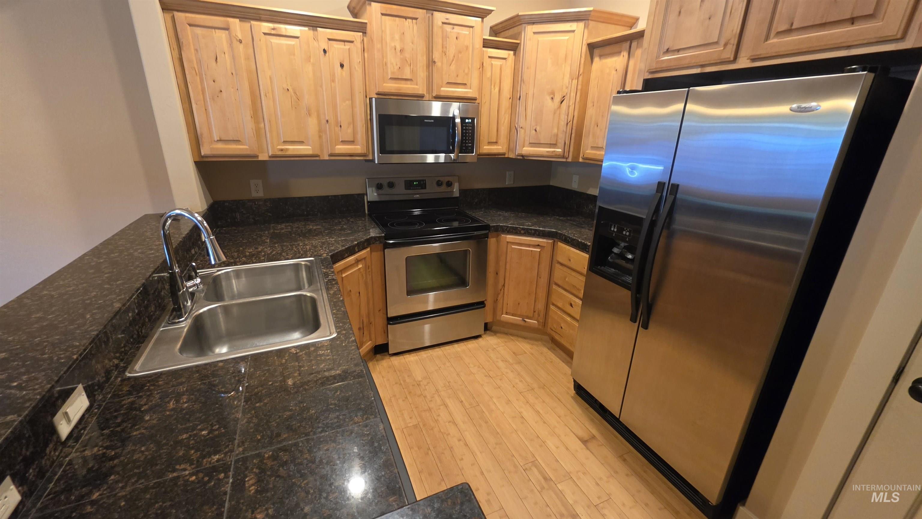 5239 West Morris Hill Road Boise, ID 83706 - Photo 3 of 19 Kitchen featuring wood cabinetry, stainless steel appliances, dark stone countertops, wood-finish flooring, and a stainless steel double basin sink with a chrome faucet