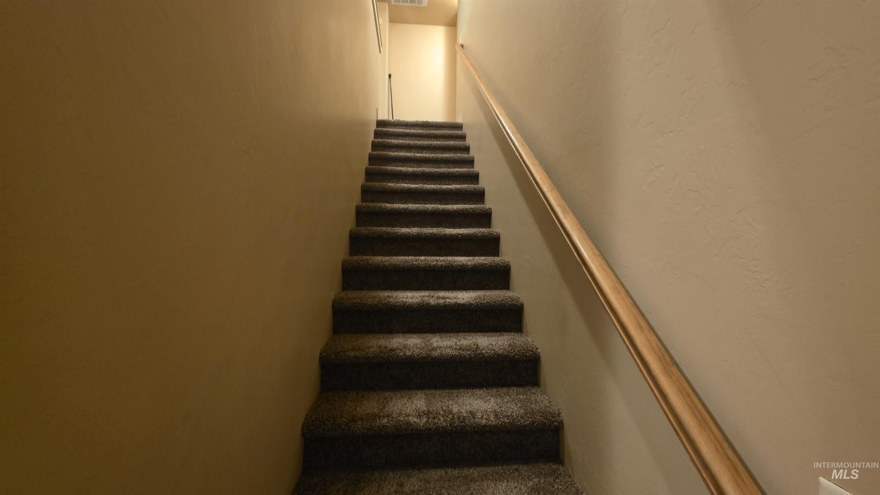 5239 West Morris Hill Road Boise, ID 83706 - Photo 5 of 19 Carpeted staircase featuring a light wood-finish handrail and neutral-toned wall finishes