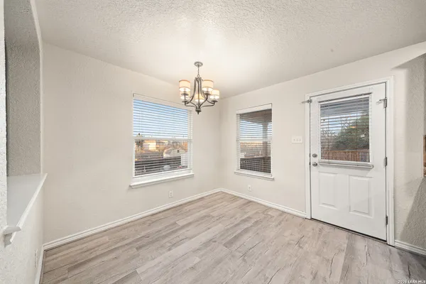 an empty room with wooden floor chandelier and windows