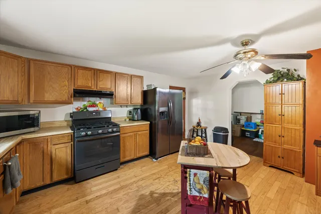 a kitchen with stainless steel appliances a stove a refrigerator a sink dishwasher a dining table and chairs with wooden floor