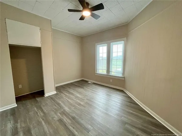 an empty room with wooden floor chandelier fan and windows