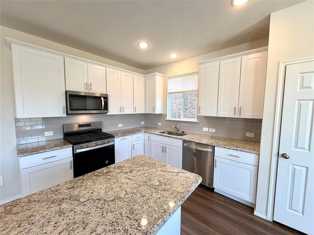 a kitchen with granite countertop white cabinets appliances and wooden floor