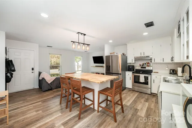 a kitchen with stainless steel appliances a stove top oven a refrigerator a sink dishwasher and a dining table with wooden floor