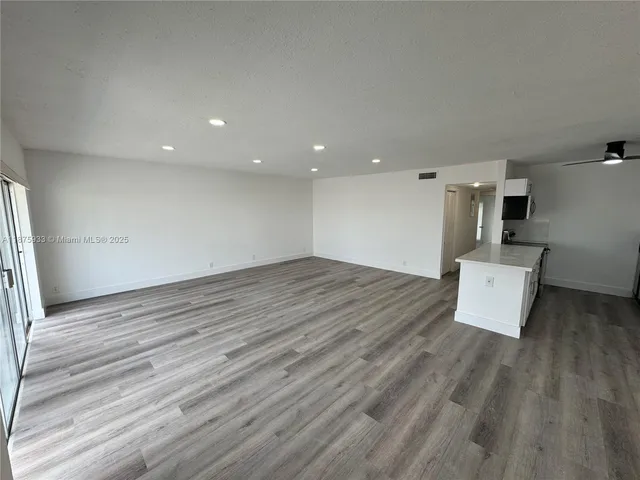 an empty room with wooden floor and kitchen view