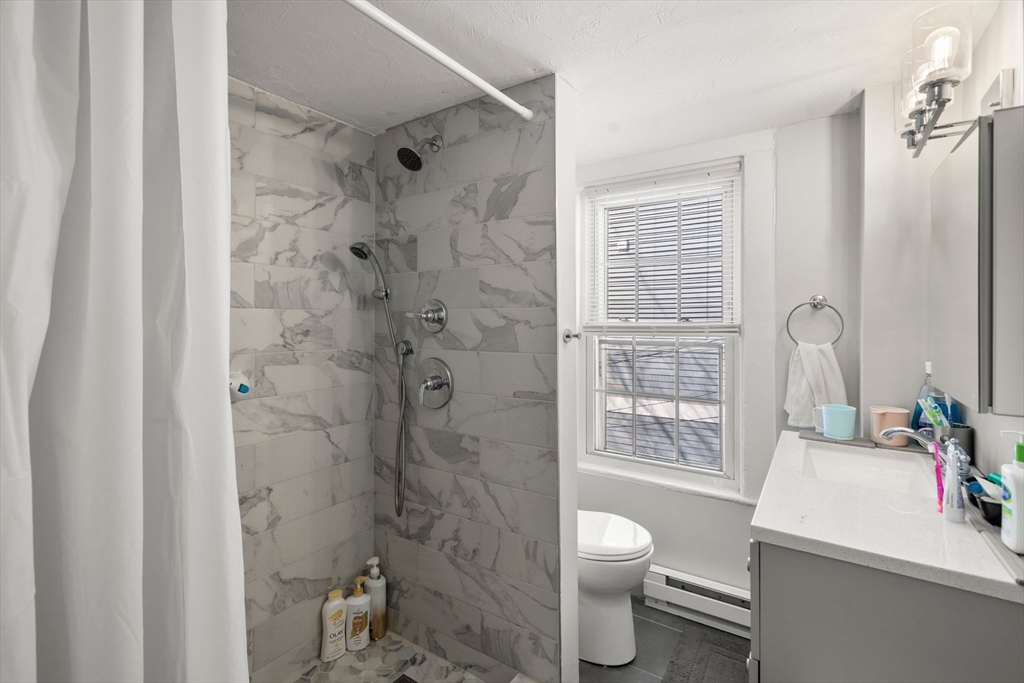 110 D Street Boston, MA 02127 - Photo 15 of 33 a bathroom with a granite countertop toilet a sink a shower and a mirror